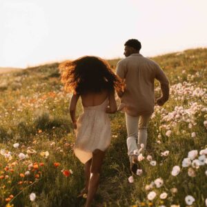 Couple courant dans un champ fleuri au coucher du soleil, illustrant la reconnexion à soi et à l’autre lors des week-ends Imago proposés par Oselience à Bois Dieu.