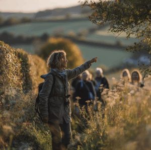 Guide nature montrant un élément du paysage à un groupe de marcheurs lors d’une randonnée au coucher du soleil.